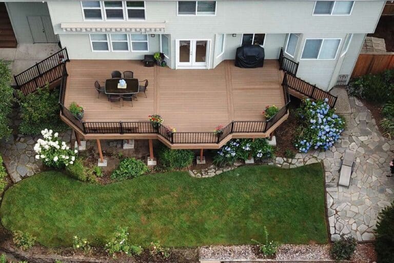 Spacious outdoor living space with a wooden deck, outdoor dining area, lush garden, and stone pathway, perfect for entertaining and relaxing in a beautiful backyard setting.