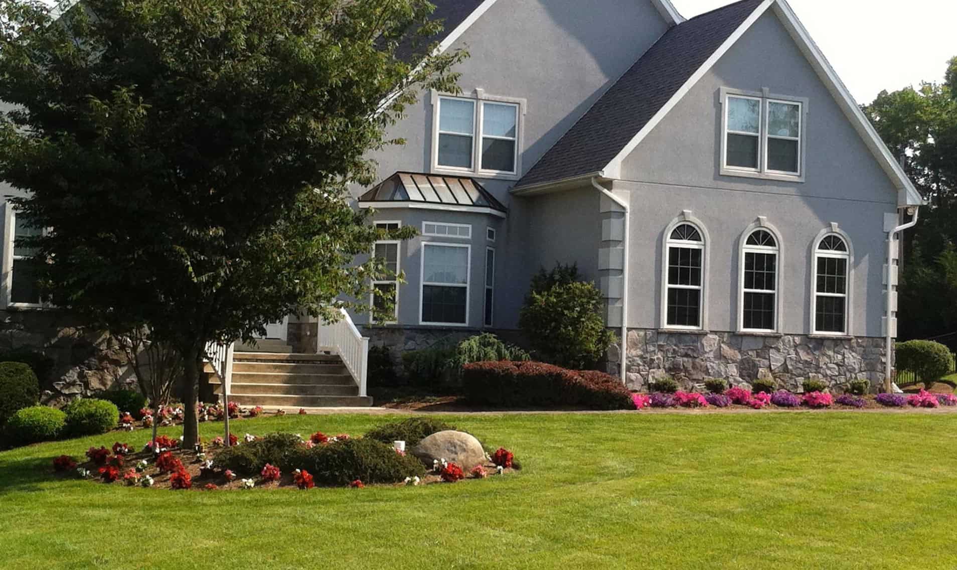 Elegant gray house with manicured lawn and colorful flower beds, showcasing beautiful outdoor living spaces and landscaping design.