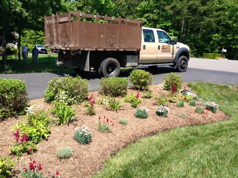 Lawn care truck and freshly landscaped flower bed showcasing outdoor living space design with vibrant flowers and landscaping.
