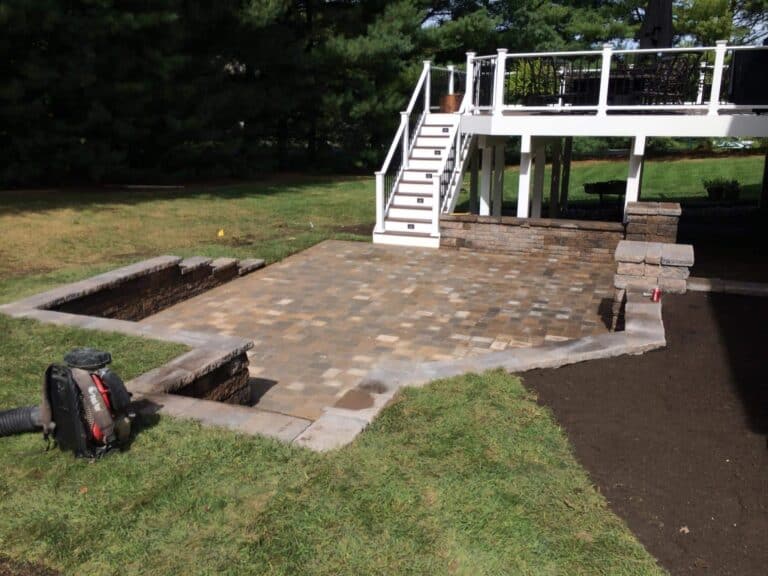 Stylish outdoor living space featuring a newly paved patio with stone pavers, a raised deck with a white railing, perfect for outdoor gatherings and relaxation.