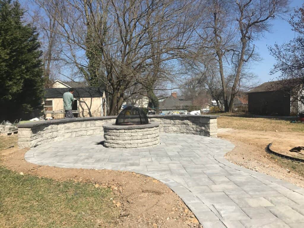 Natural stone outdoor fire pit with paved patio area, surrounded by trees and landscape for a welcoming outdoor living space.