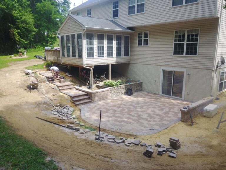 Paved backyard patio with outdoor living space under construction, brick steps, and landscaped area, featuring a spacious area ideal for outdoor gatherings and relaxation.