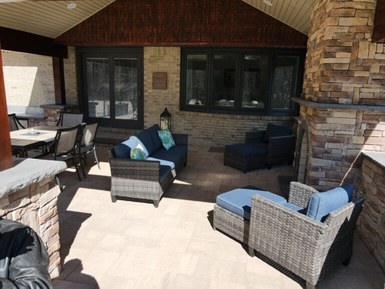 Stylish outdoor living space with comfortable wicker seating, beautiful brickwork, and a cozy fireplace, perfect for relaxing and entertaining in your backyard.