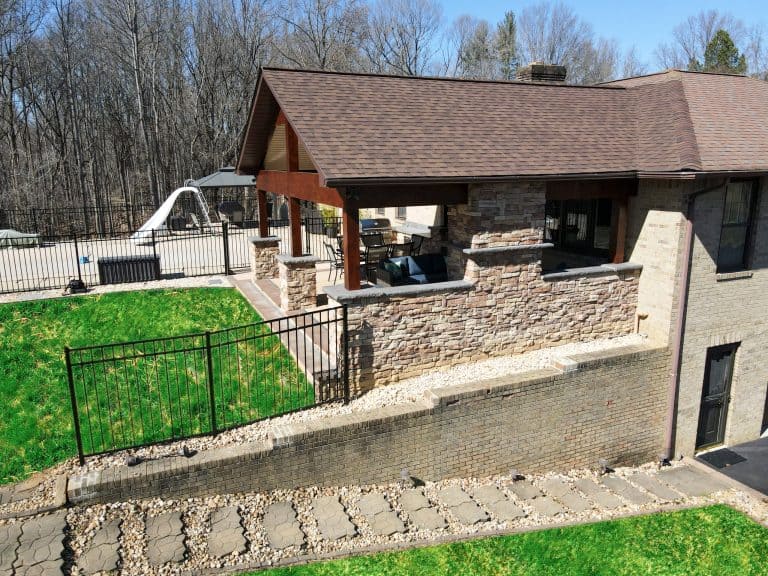 Elegant outdoor living space featuring a stone patio with seating area, a lush green lawn, and a custom retaining wall, ideal for relaxing and entertaining in a backyard oasis.