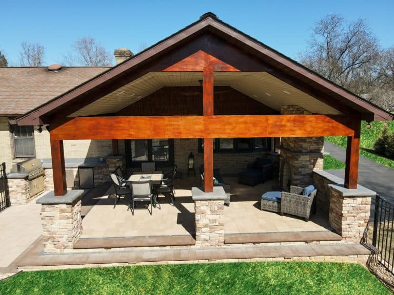 Stylish outdoor living space with a covered patio, stone pillars, and comfortable seating, perfect for entertaining guests and enjoying nature.