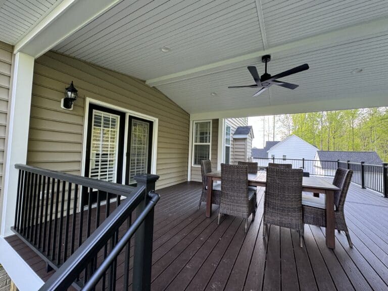 Stylish outdoor living space featuring a spacious deck with durable wood flooring, comfortable dining area with a large table and wicker chairs, covered ceiling with ceiling fan, ideal for outdoor entertaining and relaxation.