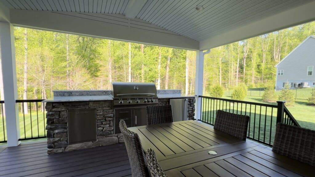 Elegant outdoor living space with built-in grill, stone accents, and a spacious deck perfect for relaxing or entertaining while enjoying lush green backyard views.