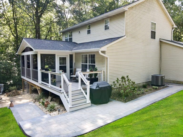 Spacious backyard with a modern screened porch, elevated deck, and lush green lawn, ideal for outdoor living and entertaining. Durable paver pathways connect the patio to the yard, surrounded by mature trees.