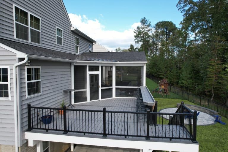 Modern outdoor living space with a spacious composite deck, black metal railings, and screened enclosure, ideal for relaxation and entertaining in a backyard with mature trees and a children's play area.