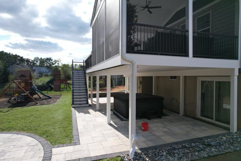 Stylish elevated outdoor living space with screened porch, spacious patio, hot tub, and play area, perfect for relaxing and entertaining in your backyard.