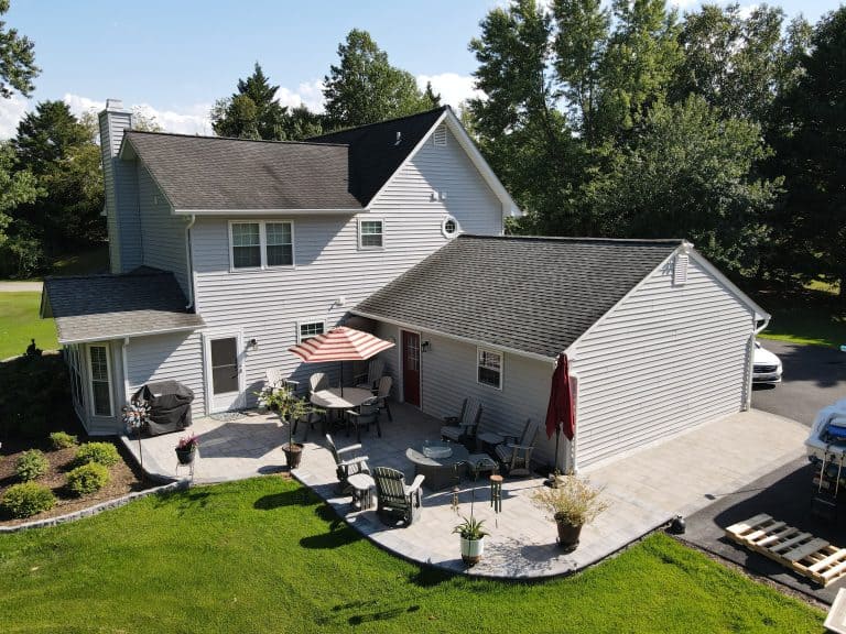 Modern backyard with spacious stone patio, outdoor furniture, dining area, and lush lawn, perfect for outdoor living and entertaining.