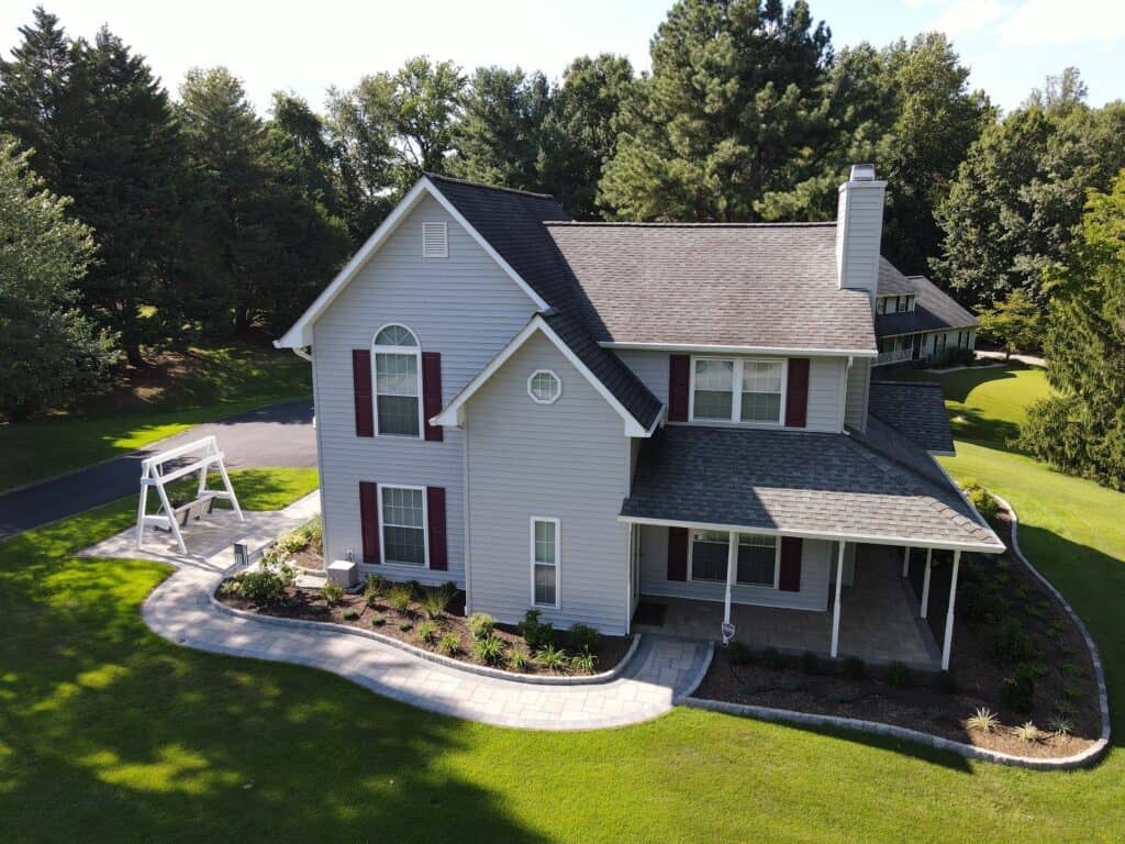 Beautiful backyard with outdoor living space featuring a paved patio, lush greenery, and a charming yard swing, perfect for relaxing and entertaining in a serene outdoor setting.