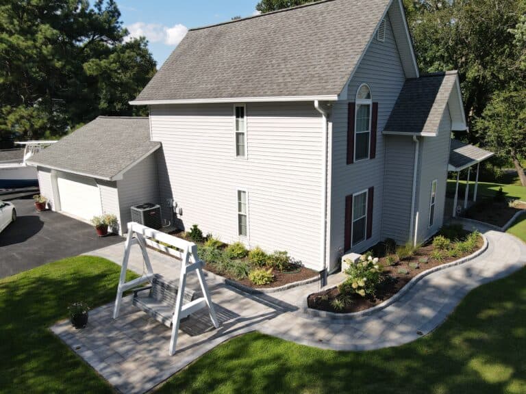 Beautiful backyard with a paved patio, white wooden swing, landscaped garden beds, and a spacious house, perfect for outdoor living and relaxing.