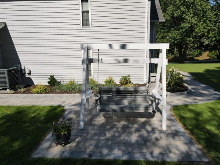 A beautiful white wooden outdoor swing with a canopy frame, perfect for relaxing in a landscaped backyard garden surrounded by lush green grass and plants.