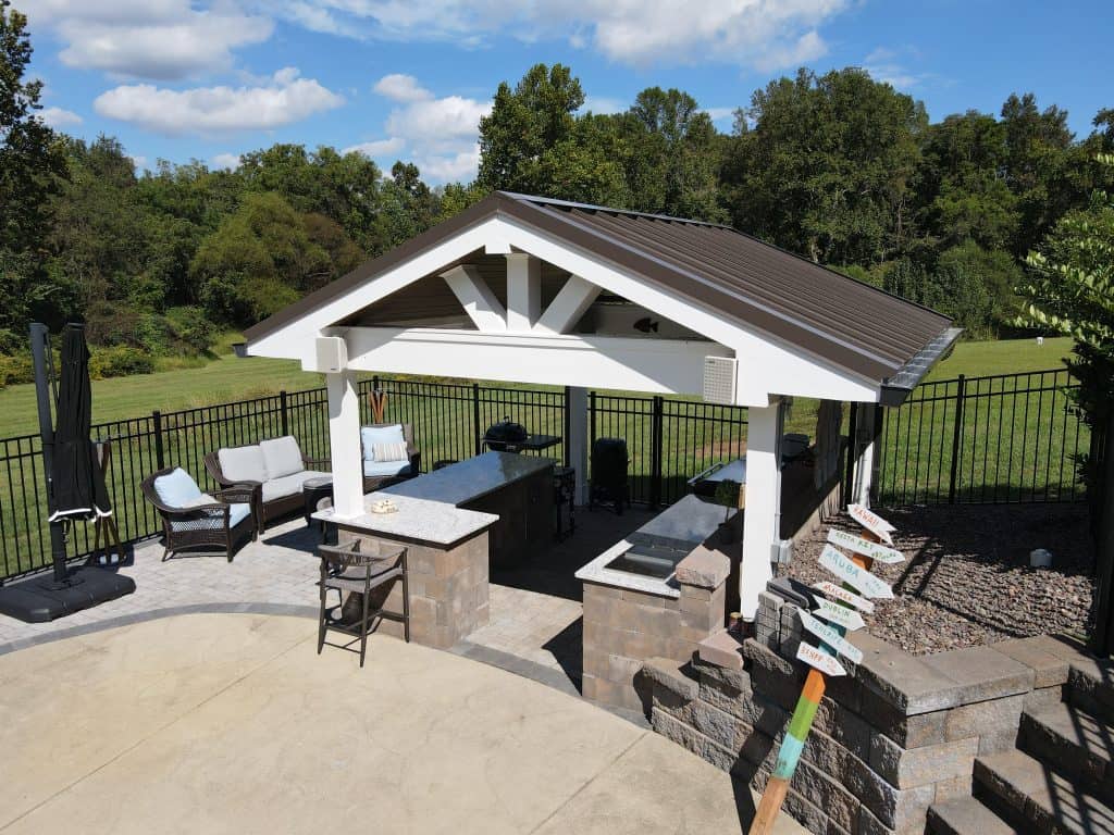 Outdoor kitchen with a bar counter, seating area, and built-in grill under a modern gazebo, surrounded by green outdoor space for outdoor living and entertaining.