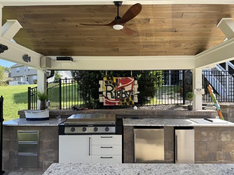 Stylish outdoor kitchen with granite countertops, stainless steel appliances, and a ceiling fan under a covered patio, perfect for outdoor living spaces and entertaining.