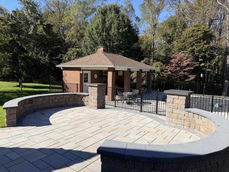 Beautiful backyard with a spacious patio, pool, and a cozy brick pavilion surrounded by lush trees and landscaping.