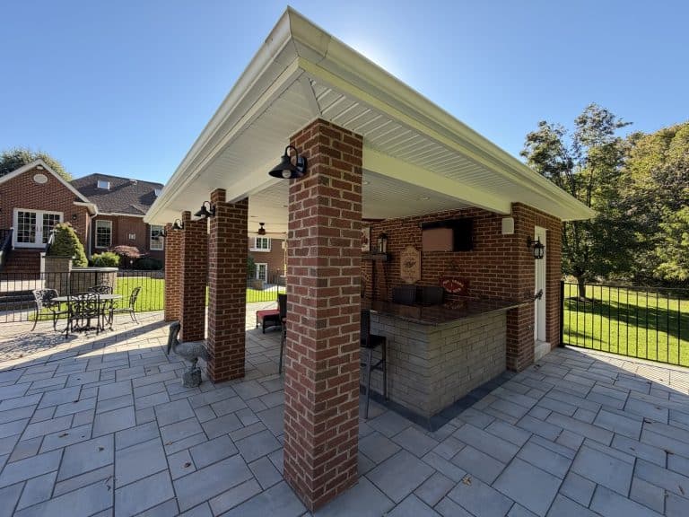 Beautiful outdoor living space featuring a brick barbecue under a covered patio with seating area and scenic backyard view.