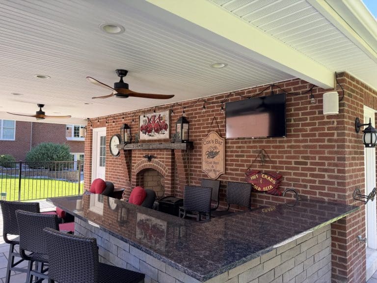 Outdoor living space featuring a brick fireplace, mounted TV, and comfortable seating with red cushions, perfect for outdoor entertainment and relaxation.