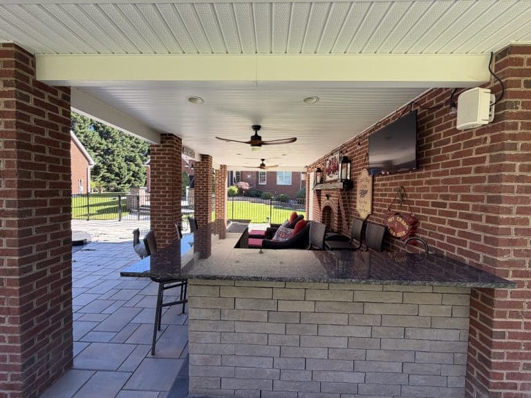 Spacious outdoor living area featuring a brick fireplace, comfortable seating, and a mounted TV, perfect for relaxing and entertaining.