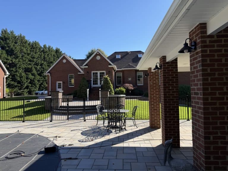 Beautiful outdoor living area featuring a spacious patio, outdoor furniture, and a view of a red brick house with lush greenery in the background.