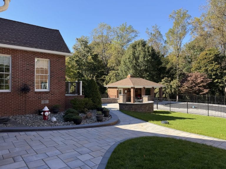 Beautiful backyard with a brick house, paved patio, swimming pool, and lush green lawn, perfect for outdoor entertaining and relaxation.