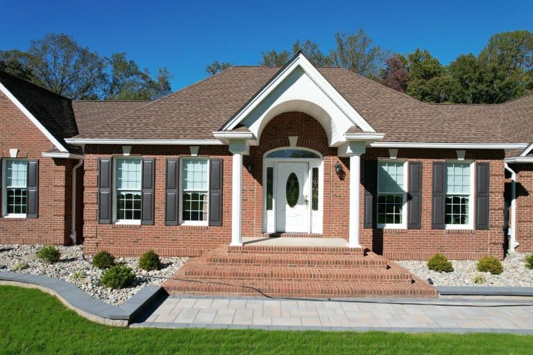 Beautiful brick house with a welcoming front porch, surrounded by well-maintained landscaping and a clear blue sky, ideal for outdoor living spaces.