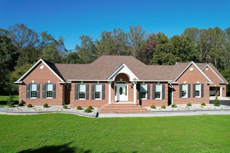 Beautiful brick house with a well-maintained lawn, surrounded by trees, under a clear blue sky, showcasing outdoor living space design.