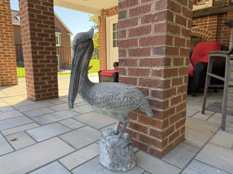 Decorative bird sculpture on patio in outdoor living space with brick columns and seating area.