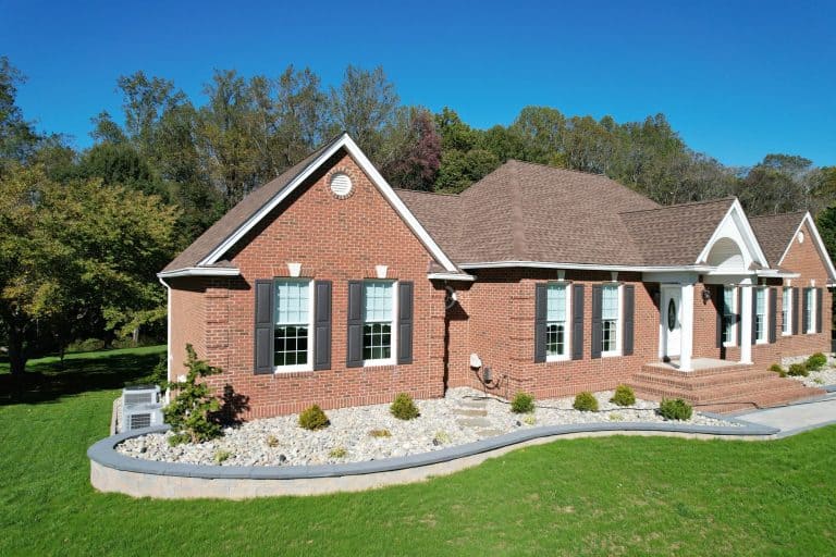 Elegant brick house with landscaped yard, perfect for outdoor living and entertaining, featuring a spacious front porch and lush green lawn.