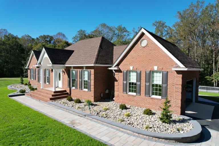 Elegant brick house with landscaped yard, paved walkway, and lush green lawn, showcasing outdoor living space design and curb appeal.