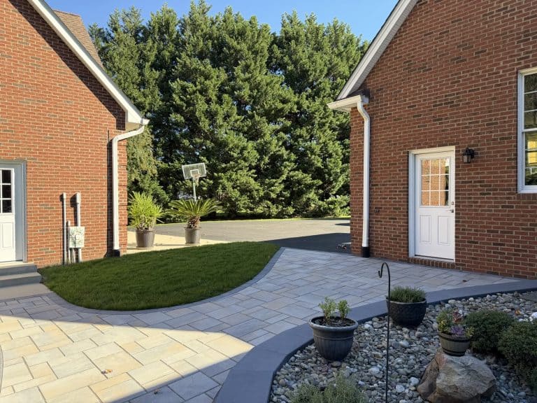 Beautiful backyard outdoor living space featuring a paved patio, lush green lawn, potted plants, and a basketball hoop, perfect for relaxation and outdoor activities.