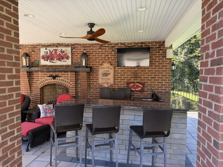 Outdoor living space featuring a brick fireplace, bar area, and seating with a ceiling fan and TV for outdoor entertainment.