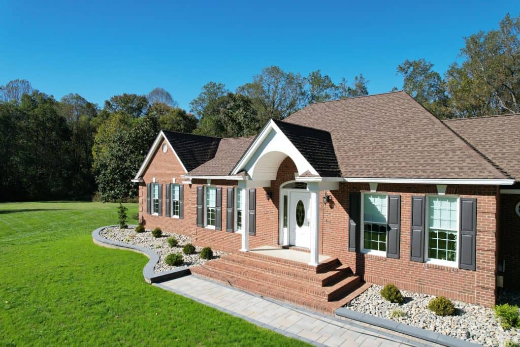 Elegant brick house with front porch, well-maintained lawn, and surrounding trees, showcasing outdoor living space design.