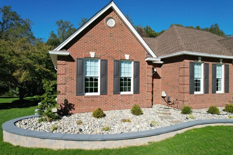 Exterior view of a brick house with well-maintained landscaping and a curved stone border in a sunny setting.